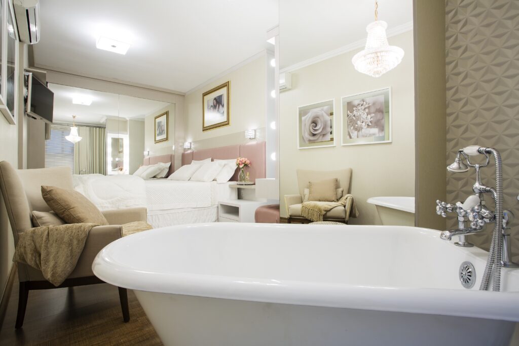 banheira de imersão estilo vitoriana dentro de um quarto com detalhes rosas e branco. a cama fica em frente a uma cama