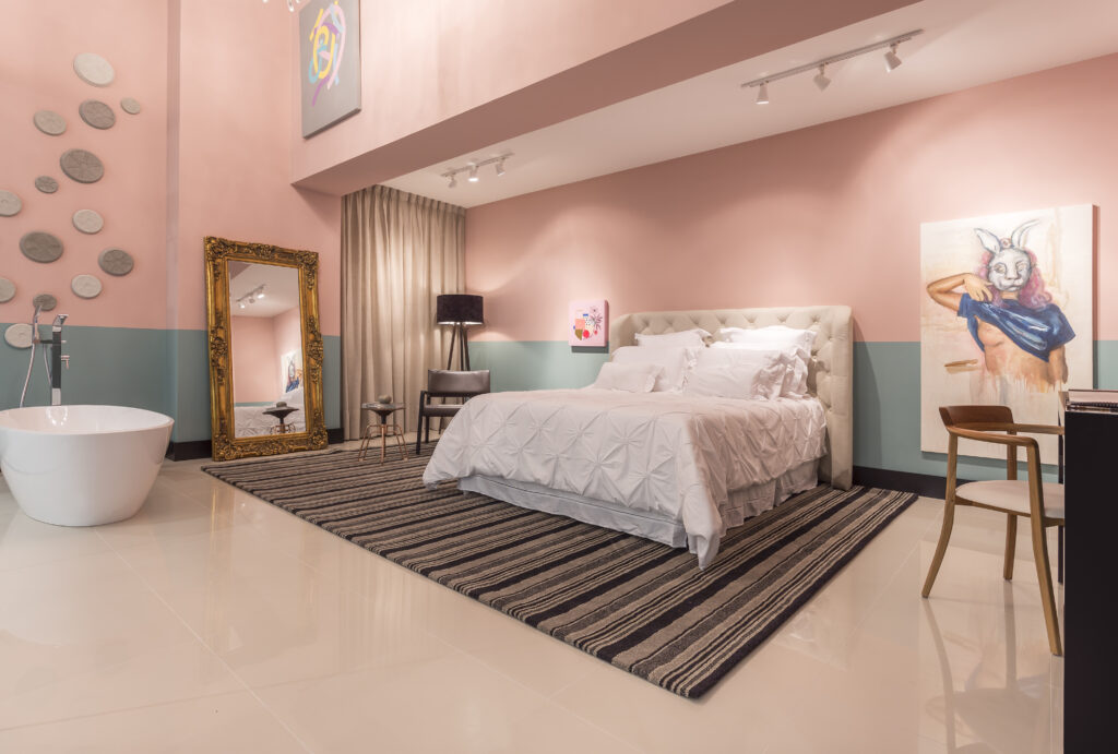 imagem de um quarto grande e amplo na cor rosa, que possui uma cama grande e uma banheira de imersão branca em frente a cama.