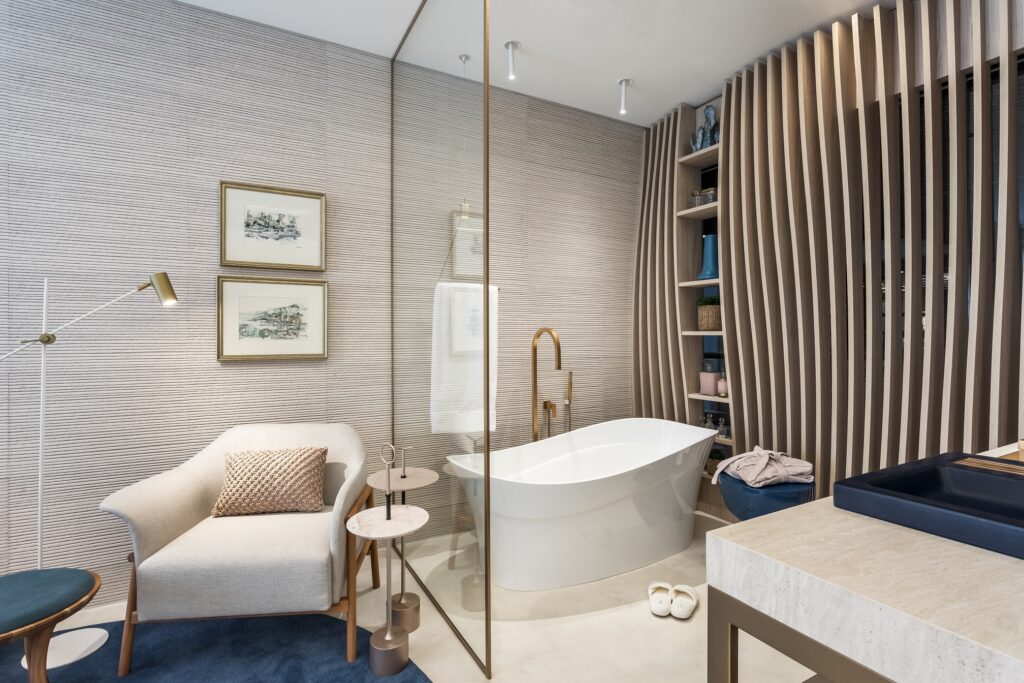Banheira de imersão branca dentro de um quarto bem decorado, com poltronas, quadros na parede e um painel de madeira com prateleiras.