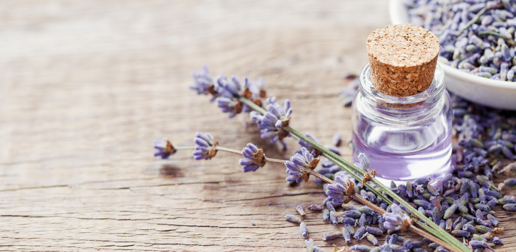 imagem de um ramo de lavanda em cima da mesa de madeira e ao lado um frasco de vidro com água dentro. ele será usado na receita de banho de imersão