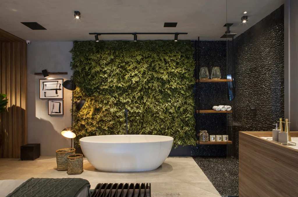 Banheira de imersão Barcelona da Doka em design freestanding branco, posicionada em banheiro luxuoso com parede verde vertical iluminada ao fundo, piso em tons neutros, área de chuveiro com revestimento preto texturizado e prateleiras de madeira com plantas no banheiro