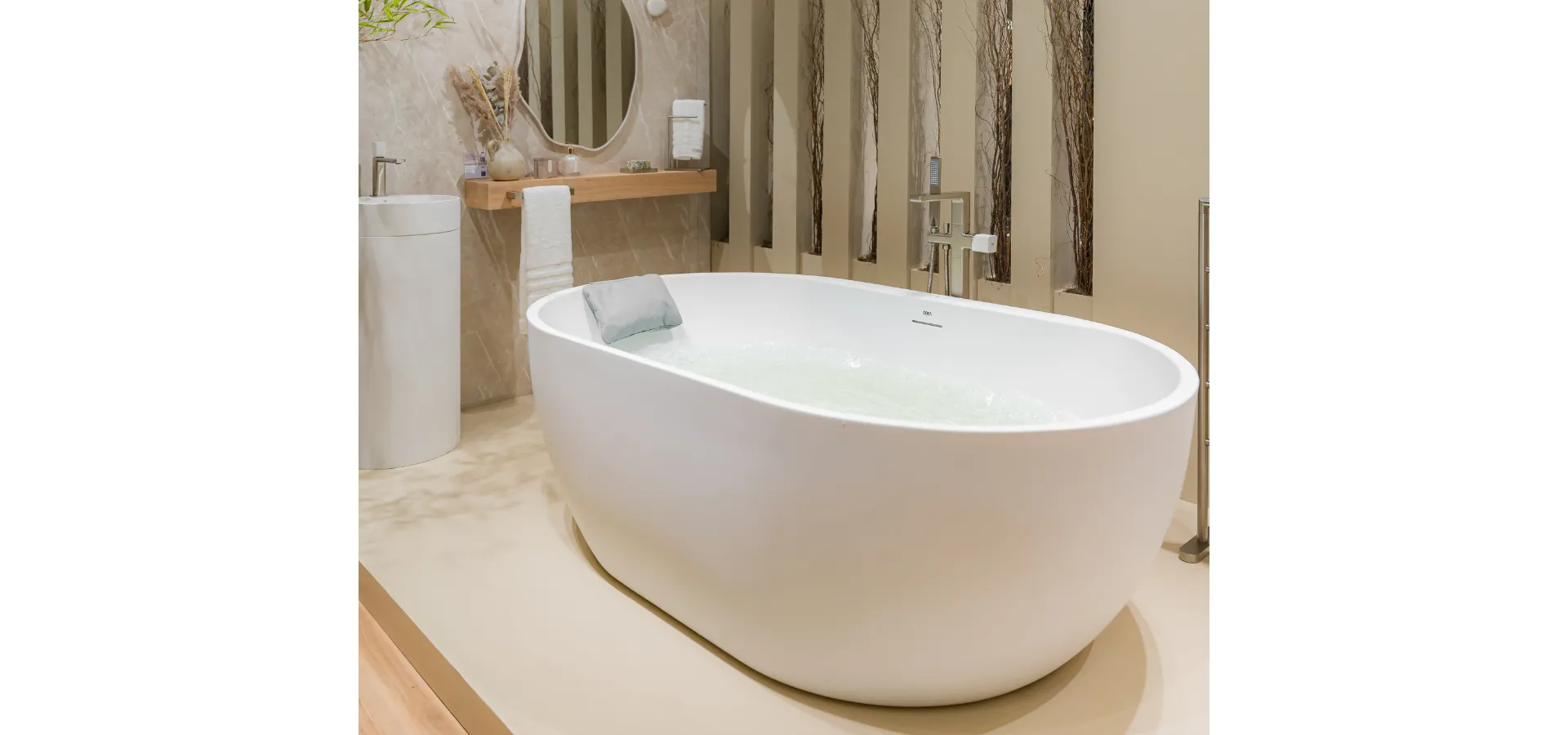 banheira freestanding Laamu X Doka preenchida com água em ambiente de alto padrão com revestimento em mármore bege, ao lado de monocomando de piso para banheira Rivvo Doka em acabamento escovado — imagem do artigo: bica ou monocomando para banheira freestanding