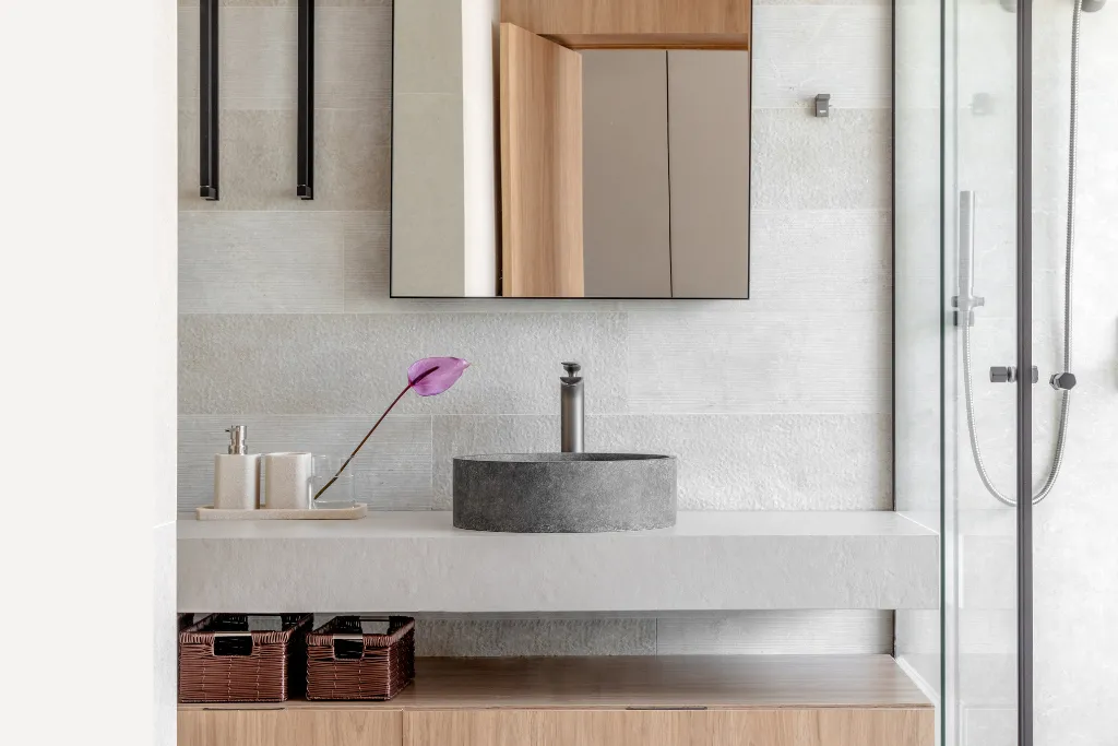 Espelho ideal para banheiro em formato retangular instalado acima da pia de apoio em pedra, com cuba redonda cinza, bancada clara e detalhes em madeira, compondo um ambiente moderno e funcional.