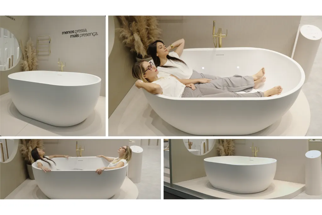 Banheira de imersão em design orgânico e minimalista, acabamento branco fosco com misturador dourado; duas mulheres relaxam na demonstração, destacando a tendência de bem-estar, autocuidado e rituais de banho para 2026.